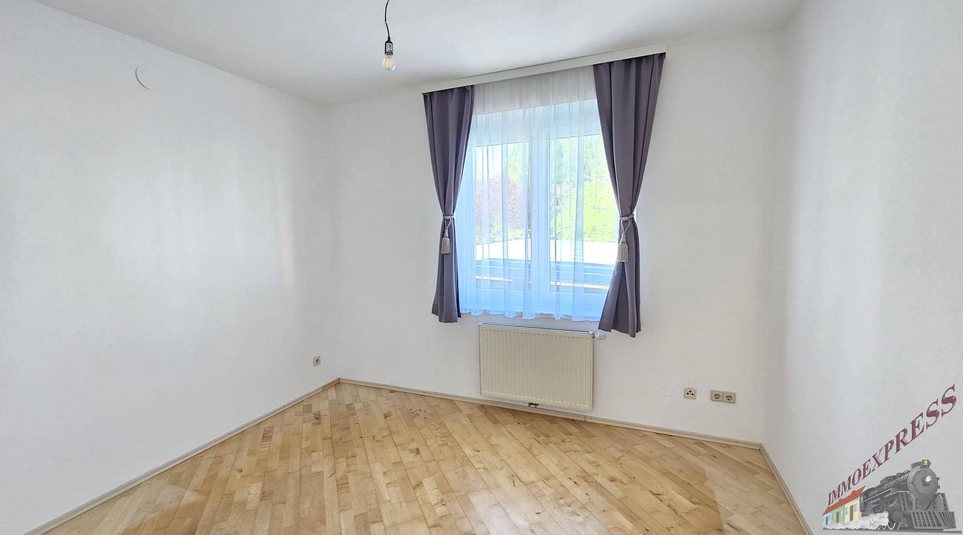 Weiteres Schlafzimmer mit Parkettboden und einem Fenster, das viel Tageslicht hereinlässt.