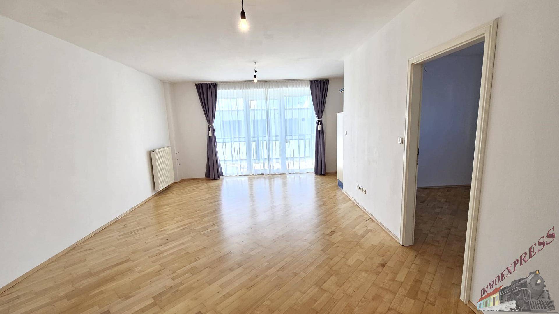 Geräumiges Wohnzimmer mit Parkettboden und großen Fenstern, die den Raum erhellen.