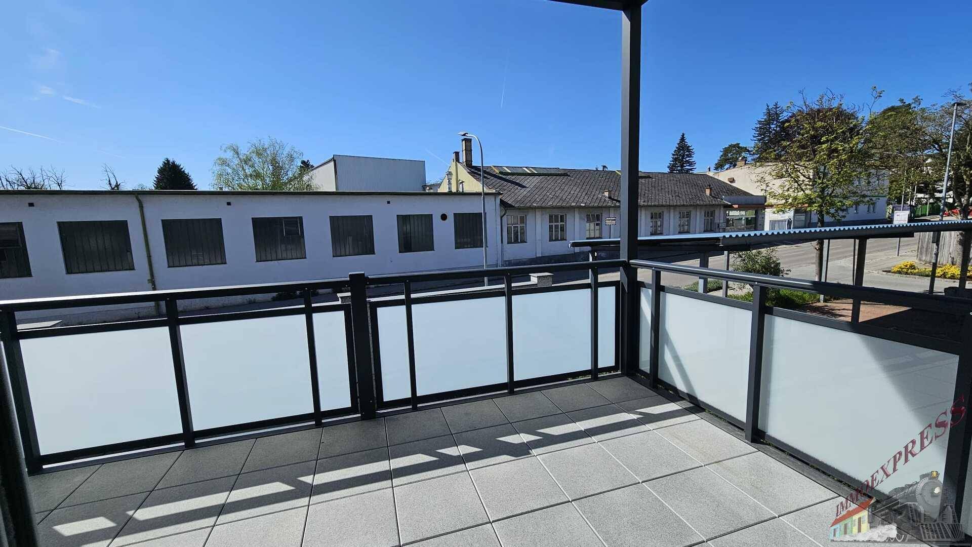 Überdachter Balkon mit Fliesenboden und moderner Glasbrüstung.