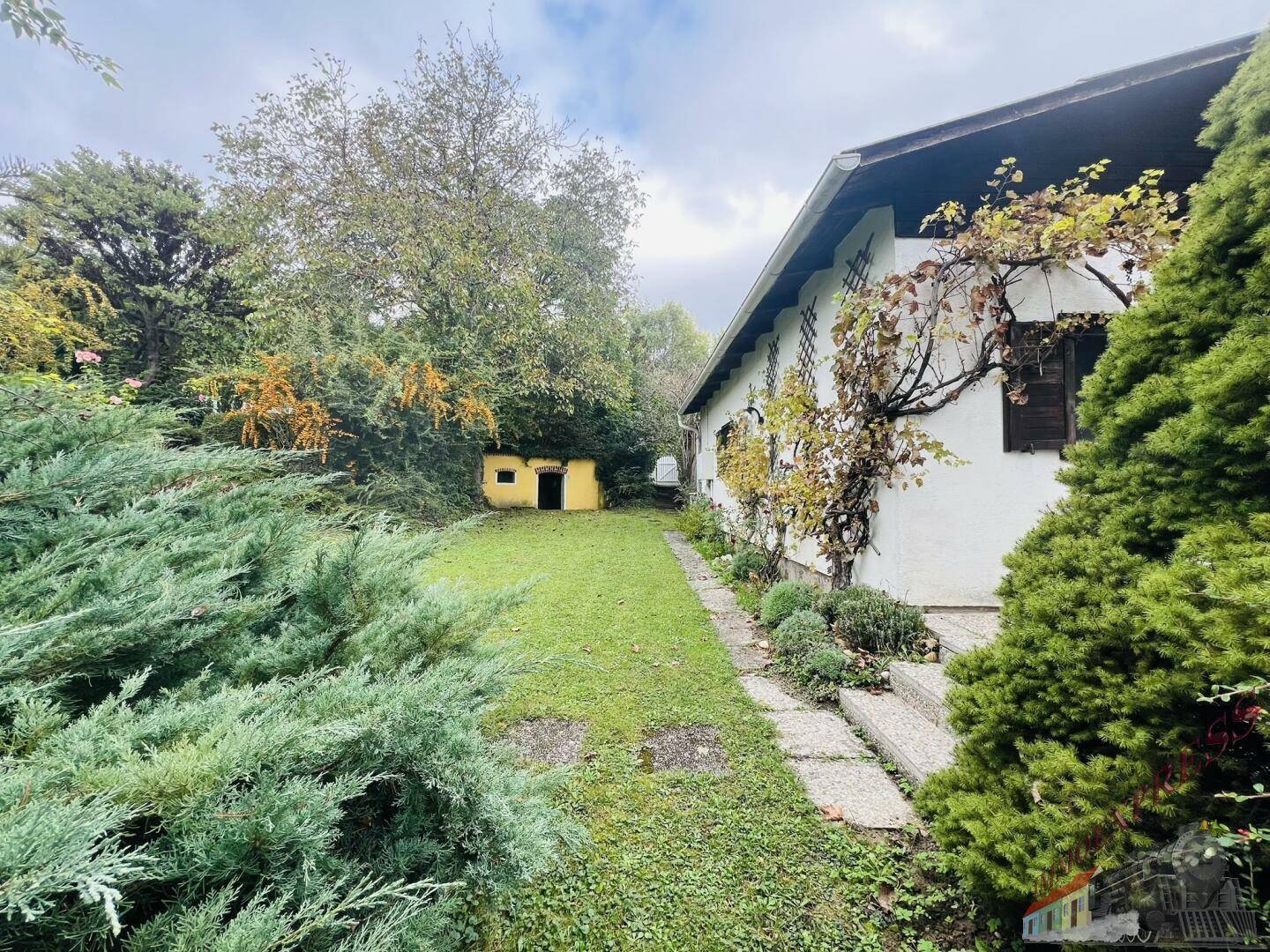 Seitlicher Gartenbereich des Hauses mit Rasenfläche, Bäumen und einem kleinen Schuppen.