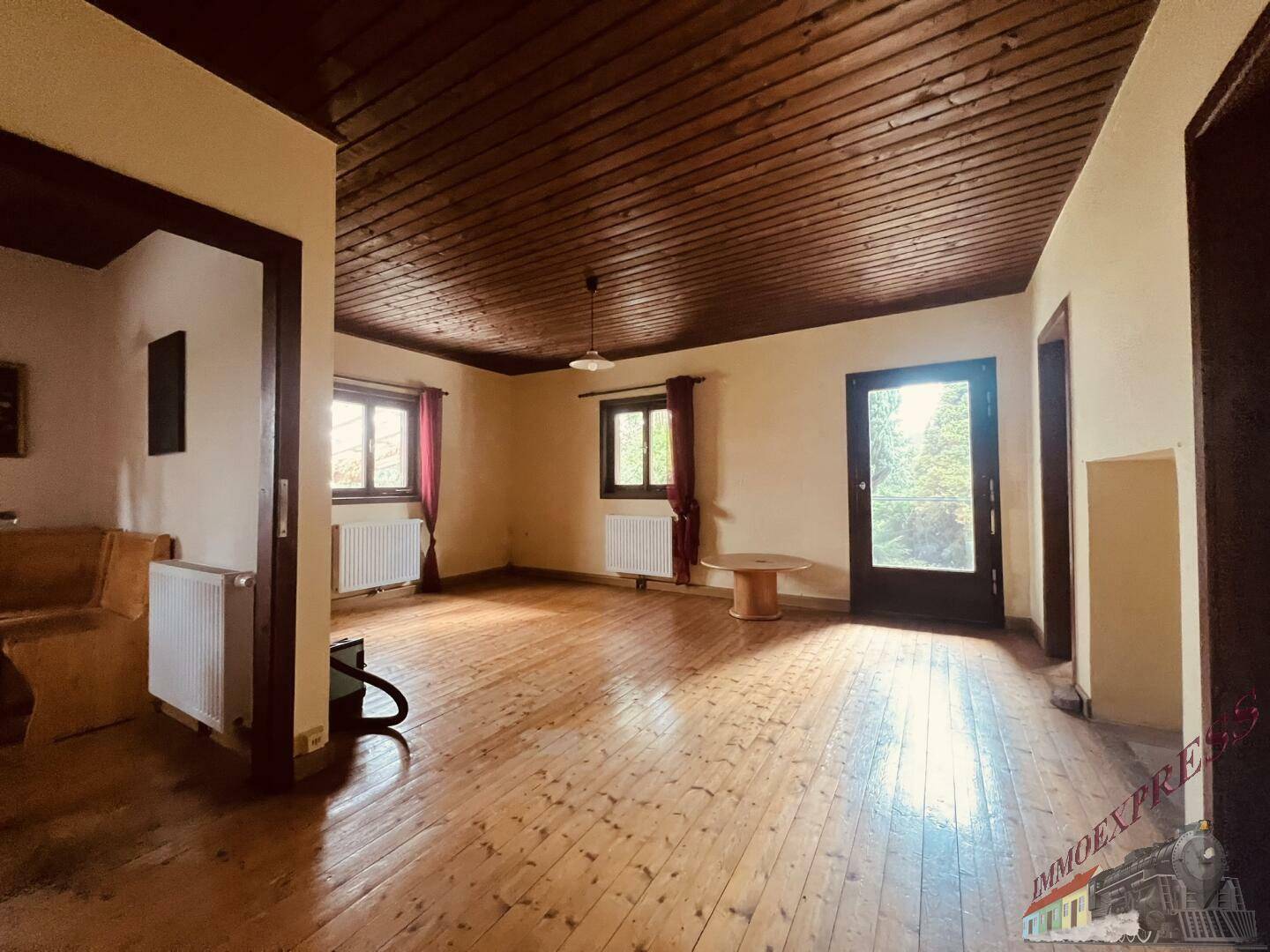 Geräumiges Wohnzimmer mit Holzdielenboden, Holzdecke und Blick in den Garten.