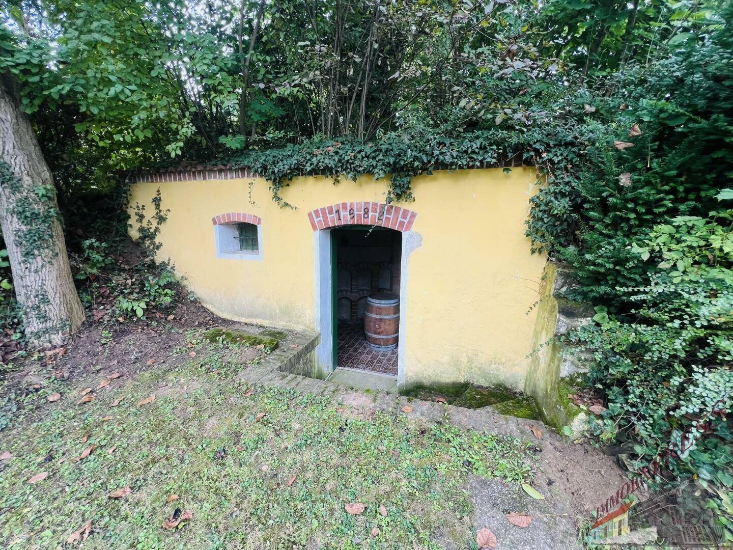 Historischer Weinkeller, eingebettet in einen bewachsenen Hügel, mit gelber Fassade und Ziegelbögen.
