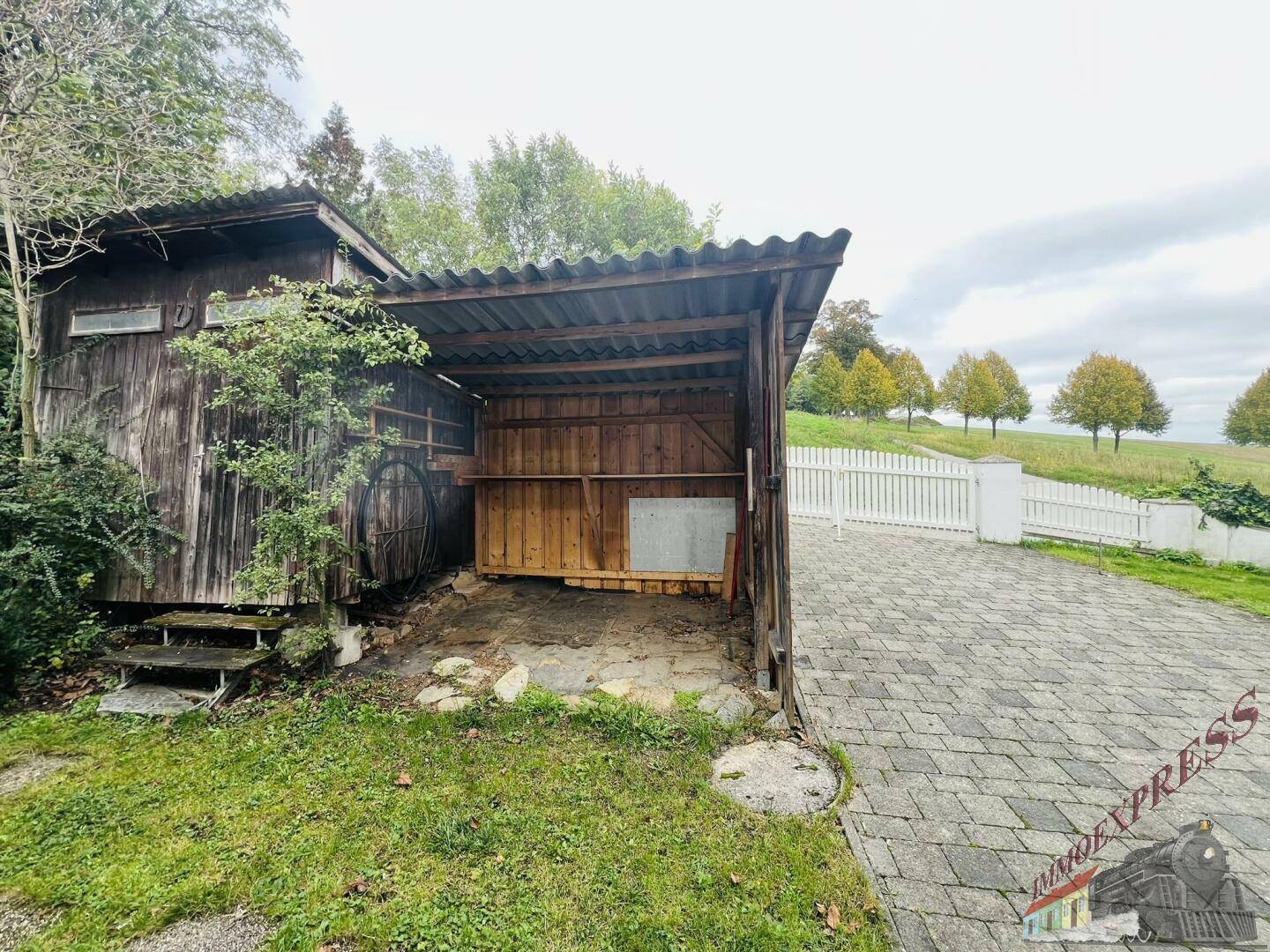 Rustikaler Holzschuppen mit Wellblechdach und angrenzendem gepflasterten Bereich.