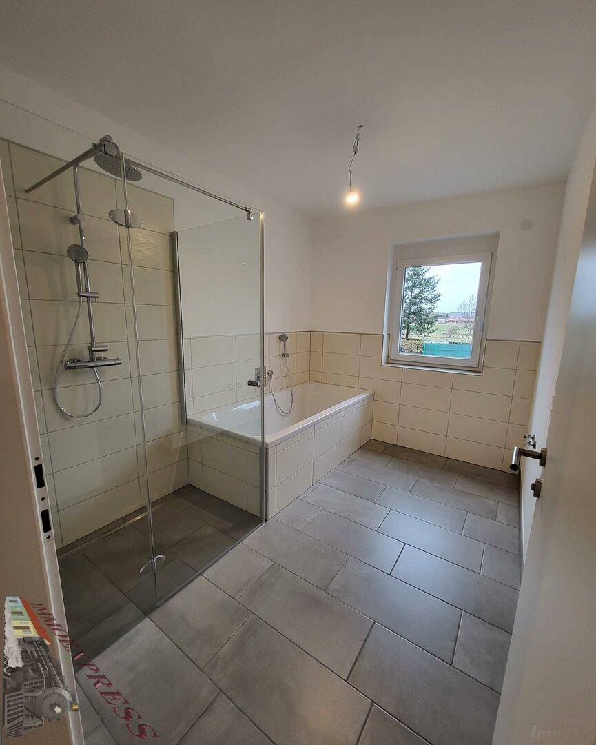 Helles Badezimmer mit Badewanne, ebenerdiger Dusche und Fenster.