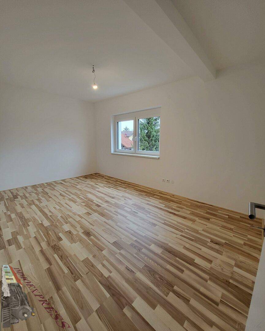 Helles Schlafzimmer mit Laminatboden und Fenster mit Blick ins Grüne.