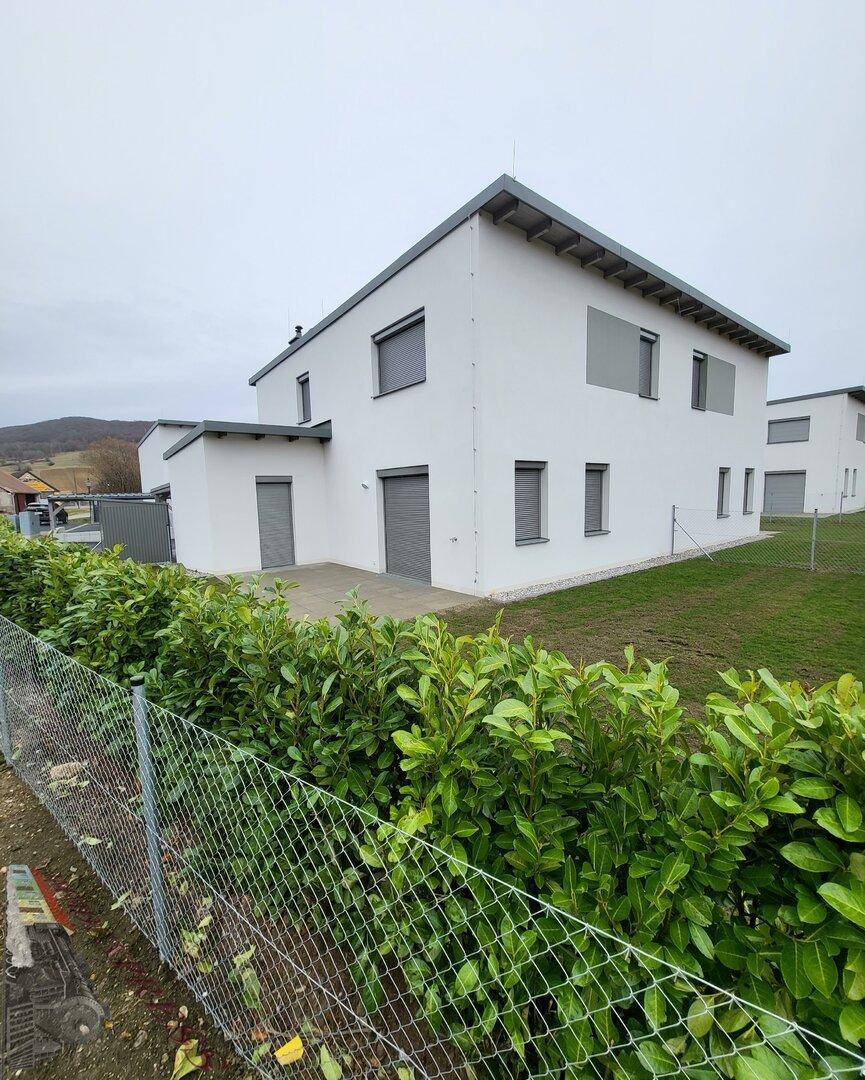 Seitenansicht der Doppelhaushälfte mit Terrasse, Garten und Blick auf die umliegende Landschaft.