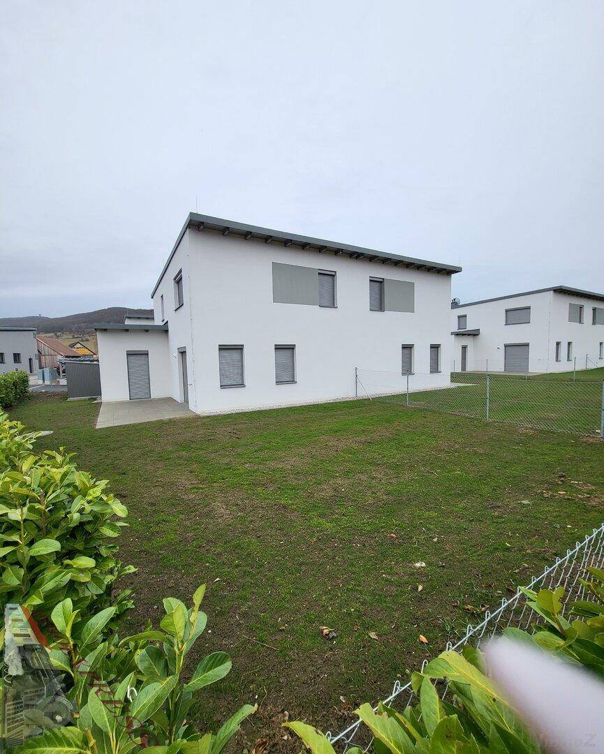Rückansicht einer modernen Doppelhaushälfte mit großem Rasenbereich und Hecke.