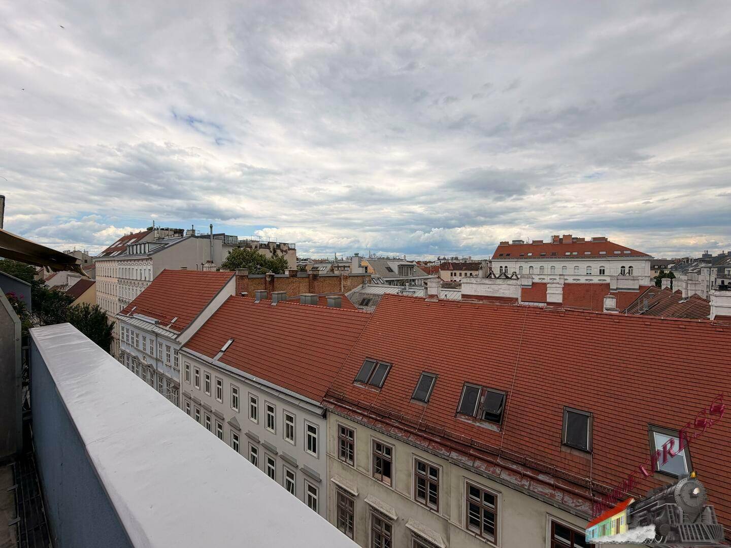 Panoramablick über die roten Dächer der Stadt und die umliegenden Gebäude unter einem bewölkten Himmel.