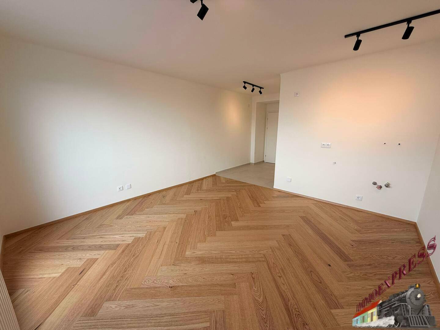 Geräumiger Wohnbereich mit hochwertigem Fischgrätparkett und schlichter, moderner Ästhetik.