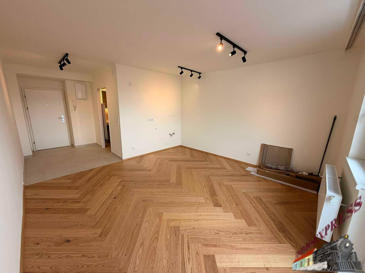 Heller Wohnraum mit elegantem Fischgrätparkett und moderner Deckenbeleuchtung, bereit zum Einzug.