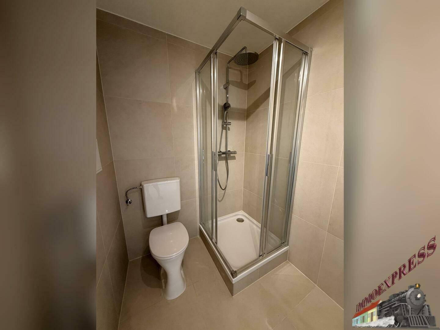 Funktionales Badezimmer mit Duschkabine, WC und durchgängiger Fliesenverkleidung in hellem Grau.
