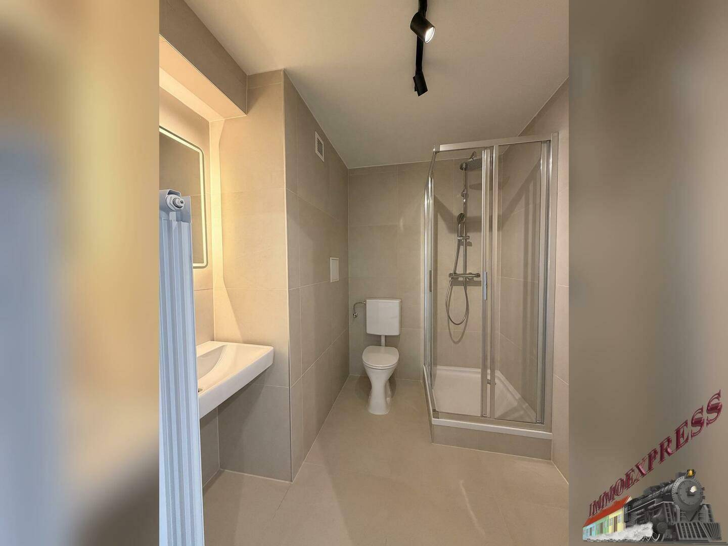 Modernes Badezimmer mit hellgrauen Fliesen, Duschkabine und wandmontiertem Waschbecken.