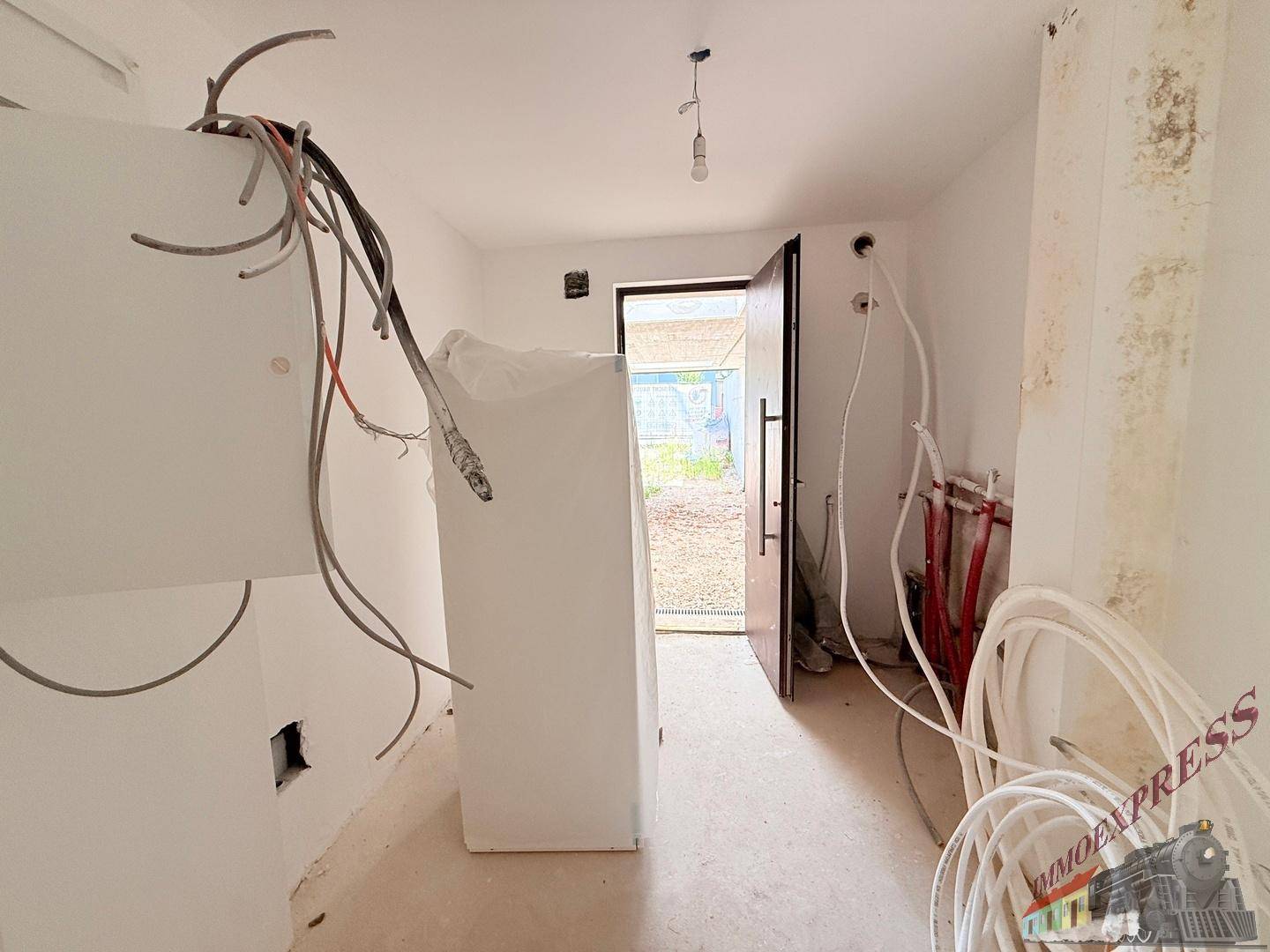 Eingangsbereich im Rohbau mit sichtbaren Installationen und Blick nach draußen.