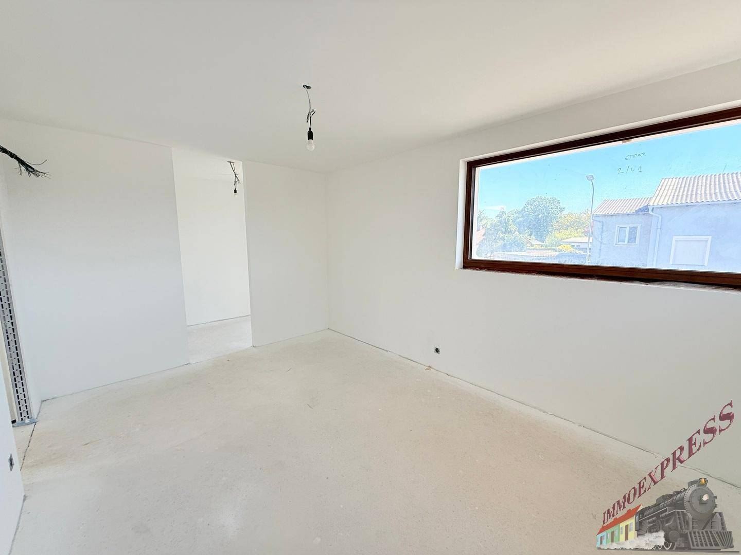 Geräumiges Zimmer im Rohbau mit breitem Fenster und Blick auf die Umgebung.