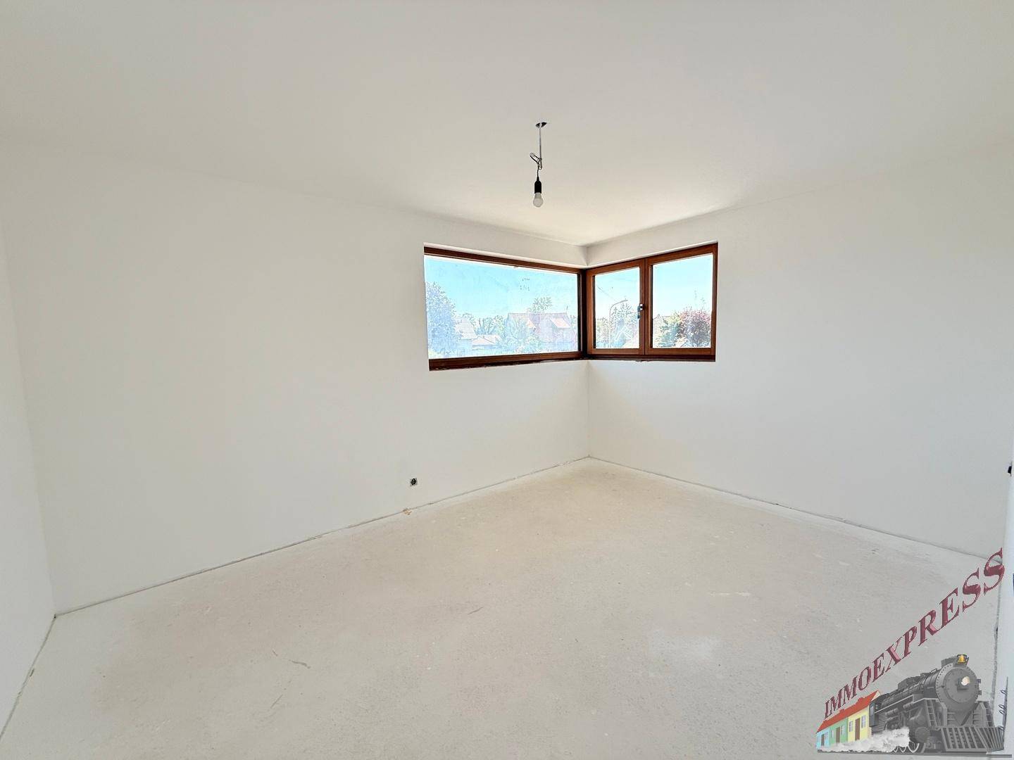 Helles Zimmer im Rohbau mit Eckfenstern, die viel Tageslicht hereinlassen.