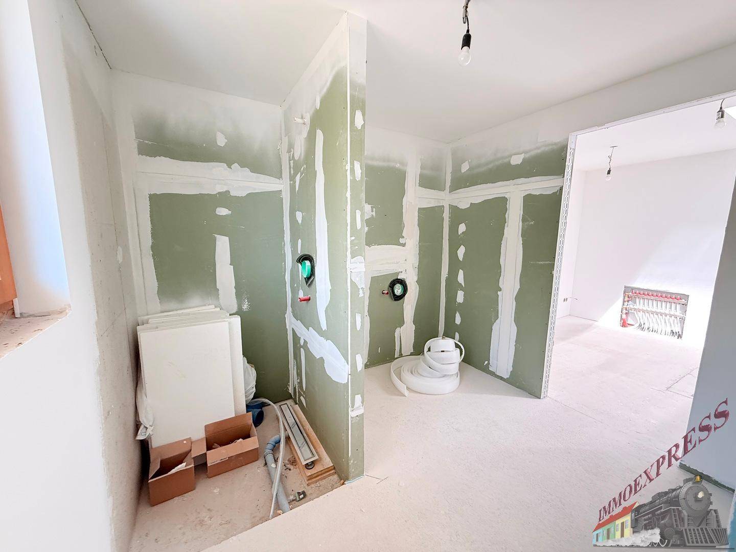 Badezimmer im Rohbau mit vorbereiteten Anschlüssen für Dusche und Waschtisch.