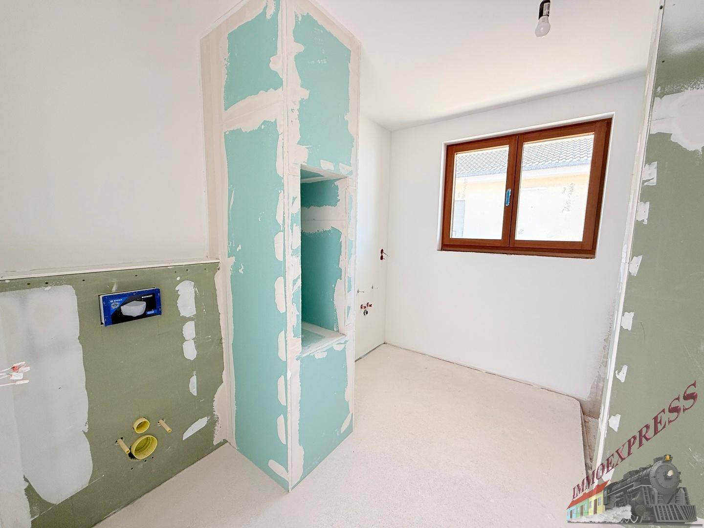 Badezimmer im Rohbau mit vorbereiteten Installationen und Fenster für Tageslicht.