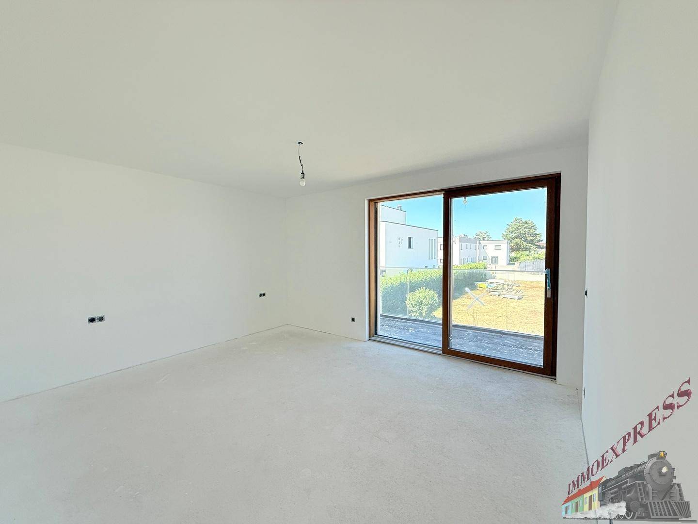 Geräumiges Schlafzimmer im Rohbau mit viel Tageslicht und Blick auf den Garten.