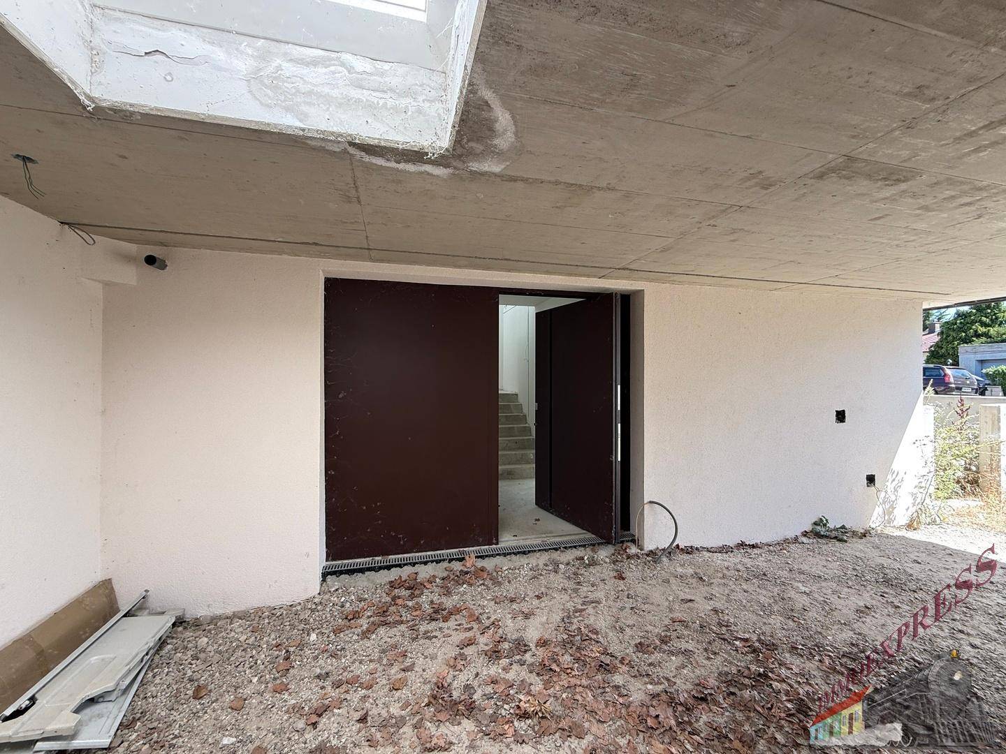 Eingangsbereich im Rohbau mit breiten Türen und Blick auf den unfertigen Außenbereich.