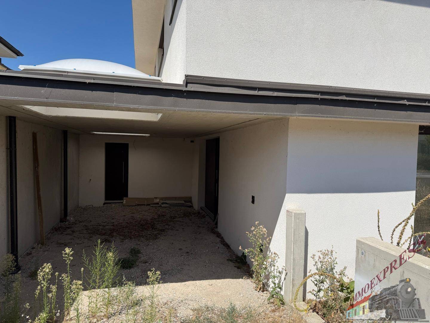 Überdachter Carport-Bereich einer modernen Doppelhaushälfte mit Zugang zum Gebäude.