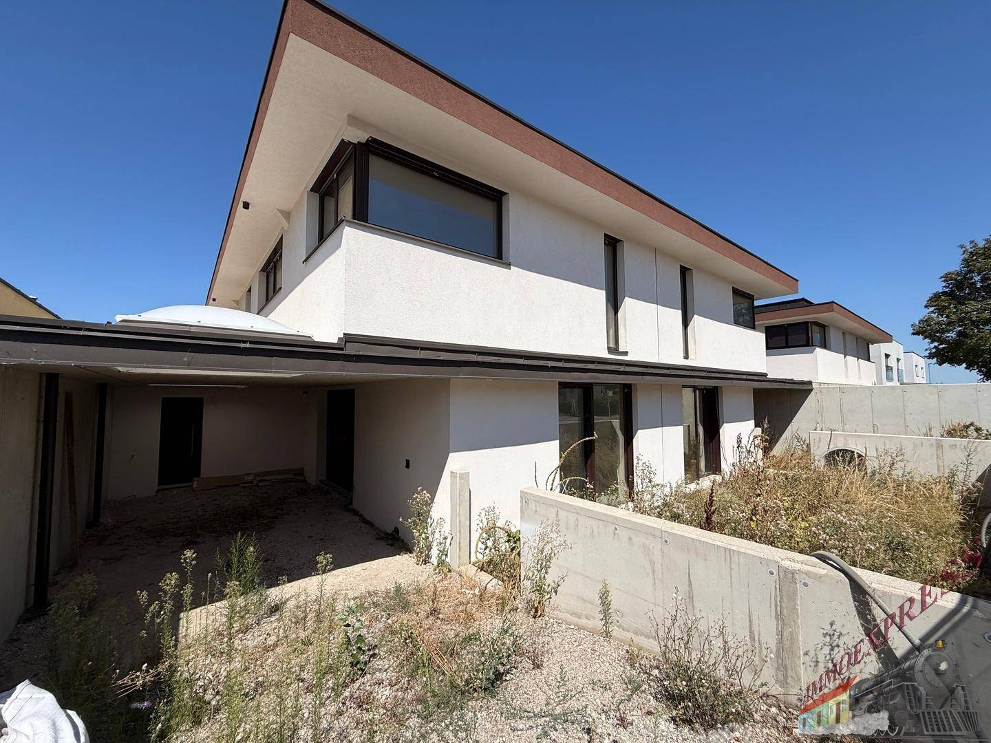 Moderne Doppelhaushälfte mit integriertem Carport und unfertigem Außenbereich unter klarem Himmel.