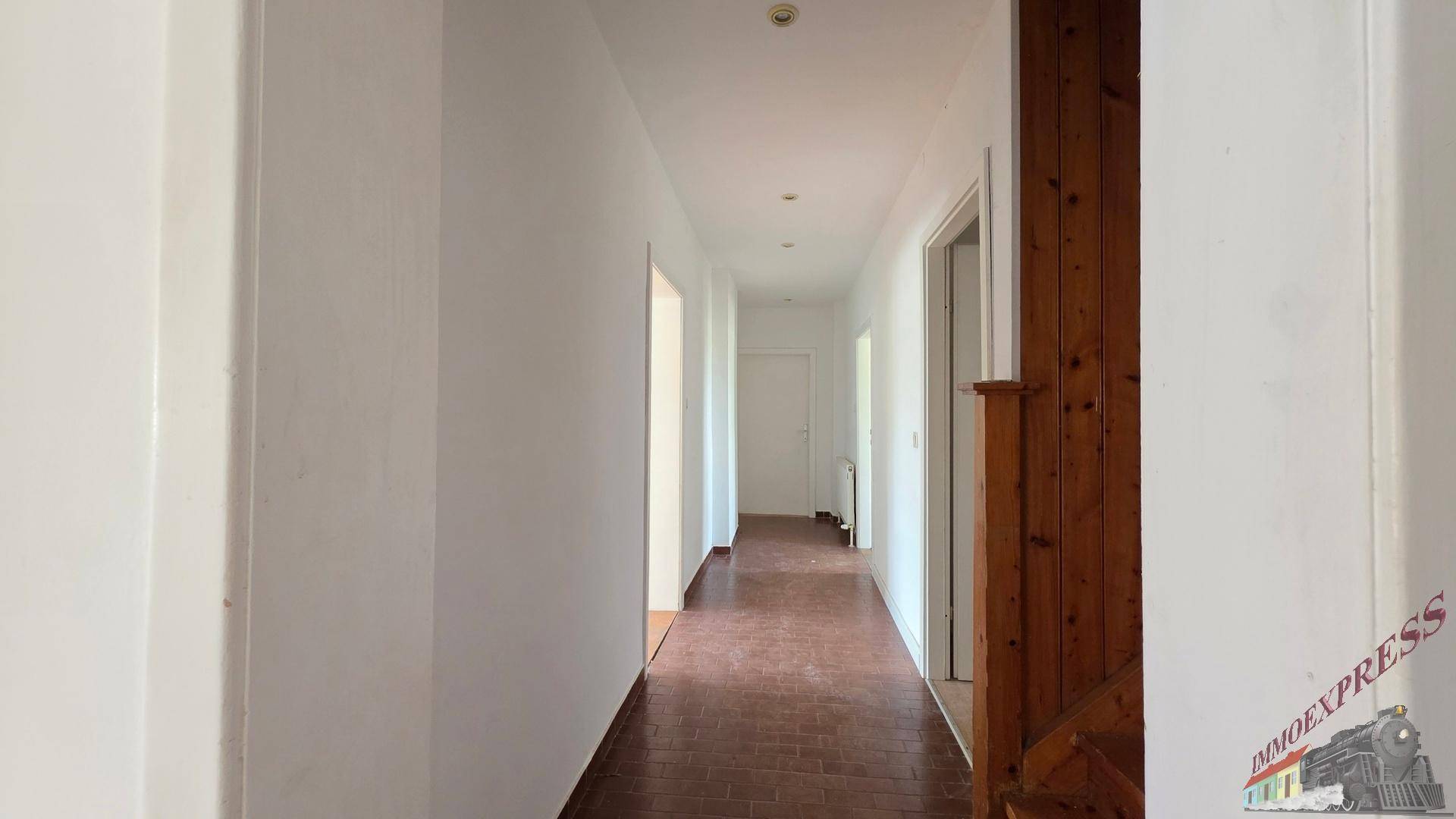 Heller Flur mit dunklem Holzboden, weißen Wänden und einer Holztür, die zu weiteren Räumen führt.