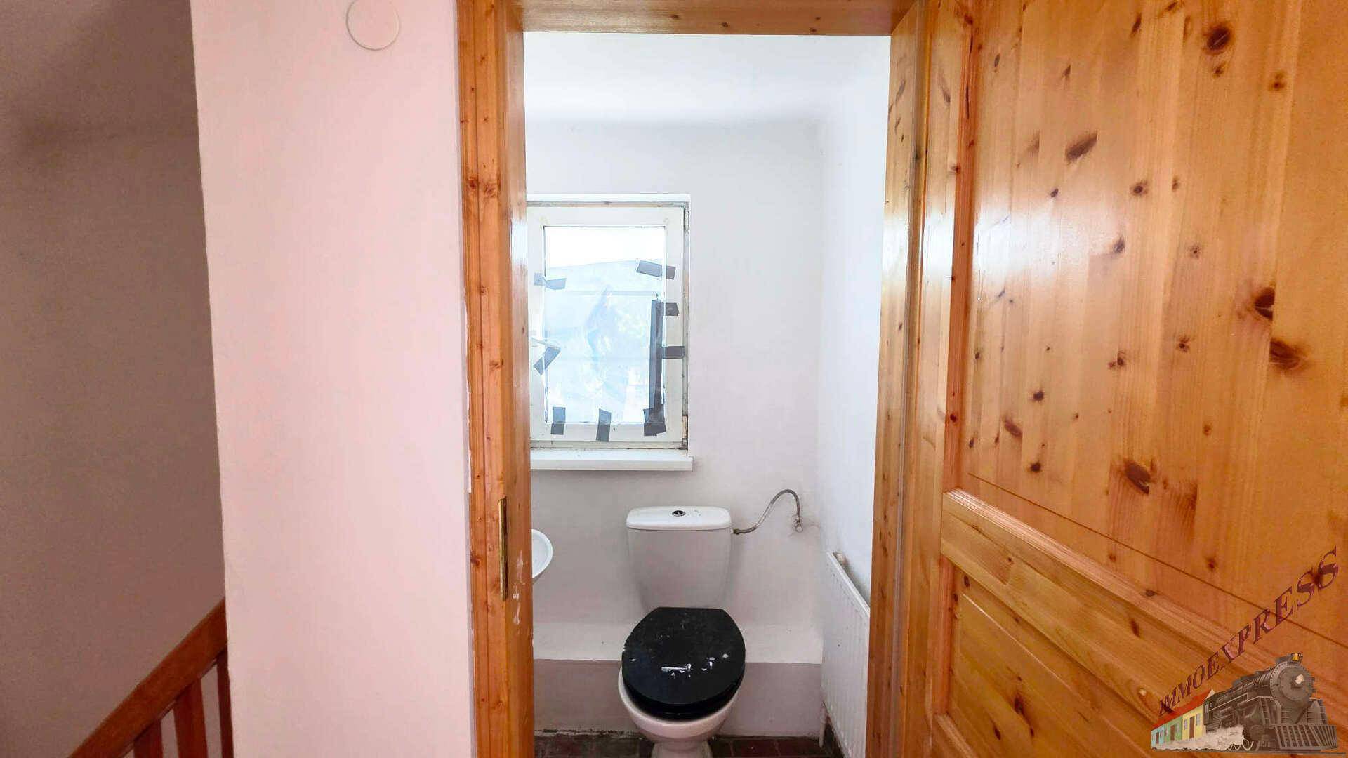 Kleines Gäste-WC mit Fenster, Toilette und Waschbecken, umgeben von Holztüren.