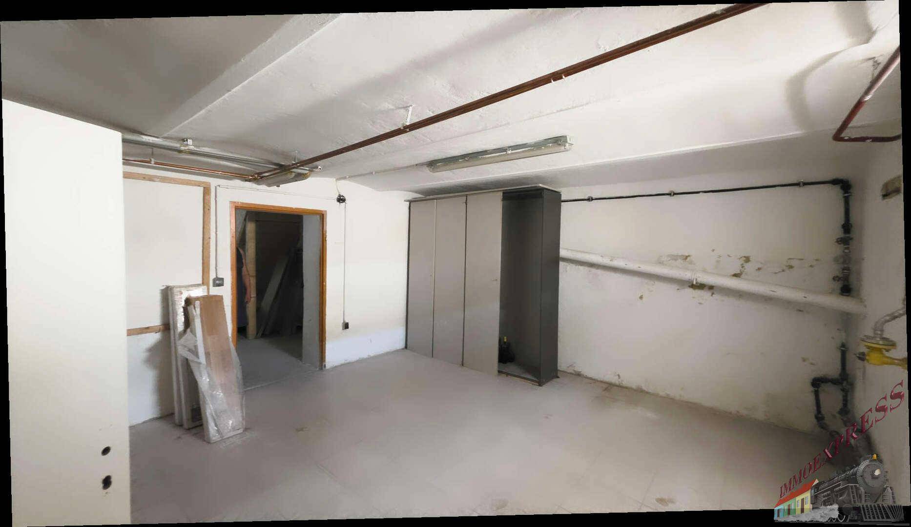 Geräumiger Kellerraum mit Betonboden, sichtbaren Rohren und einem Schrank.