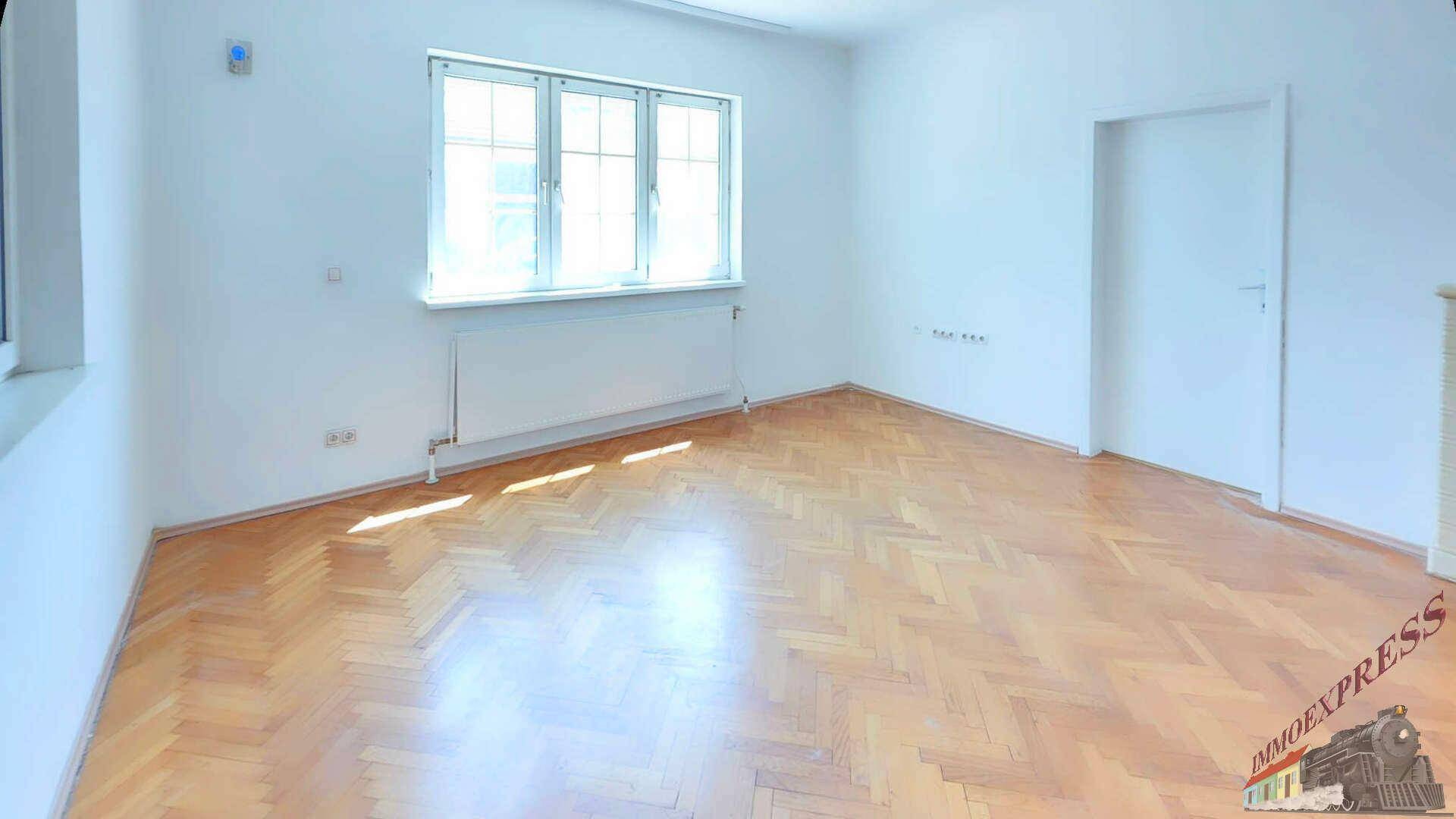 Helles Wohnzimmer mit Fischgrätparkettboden, großen Fenstern und weißen Wänden.