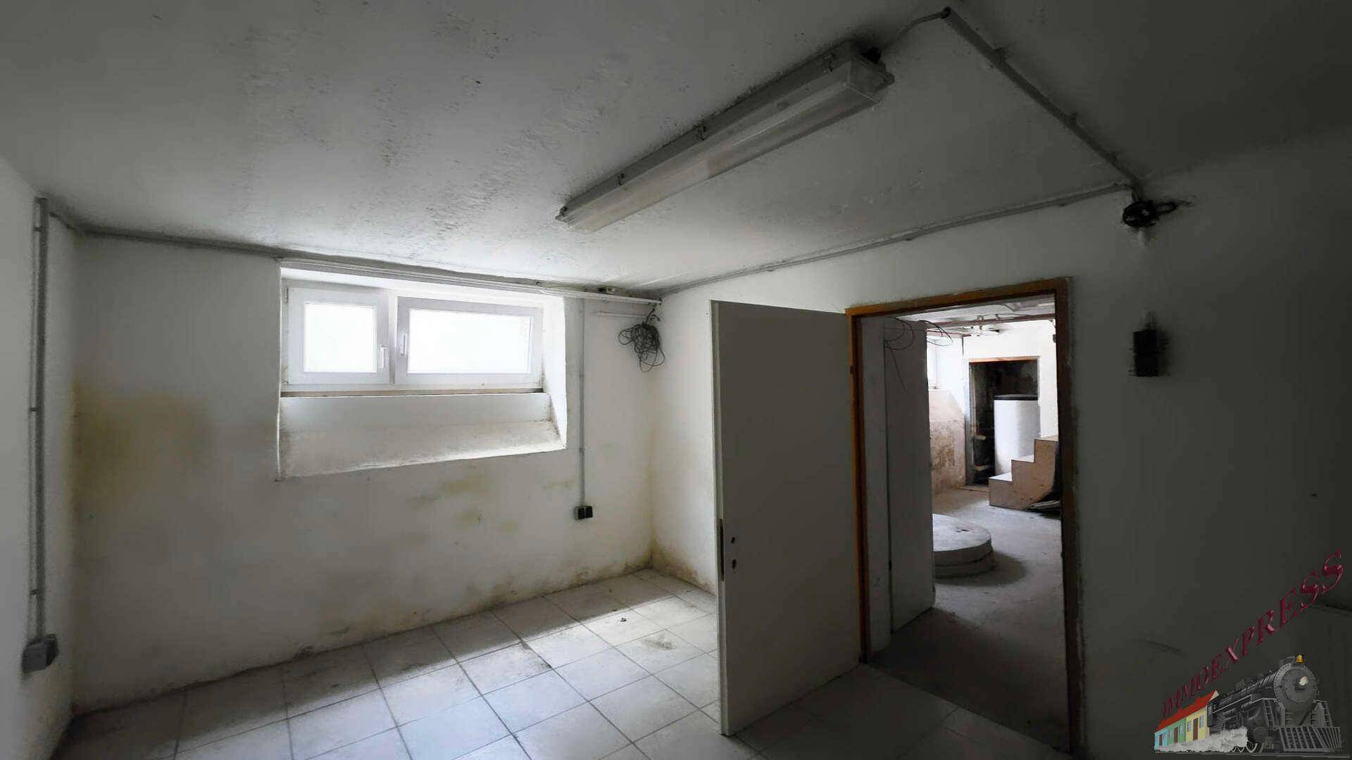 Kellerraum mit Fliesenboden, einem kleinen Fenster und einfachen Wänden.