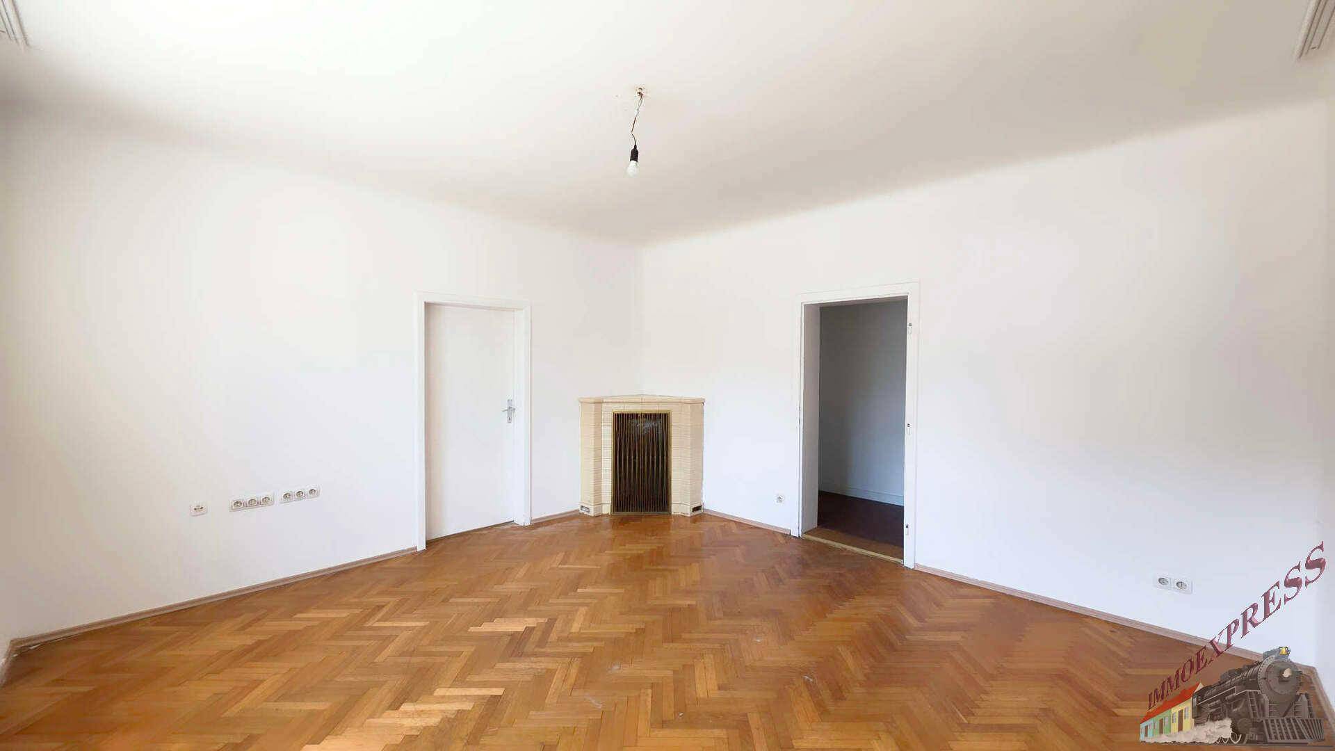 Geräumiges Wohnzimmer mit Fischgrätparkett, einem dekorativen Kamin und weißen Wänden.