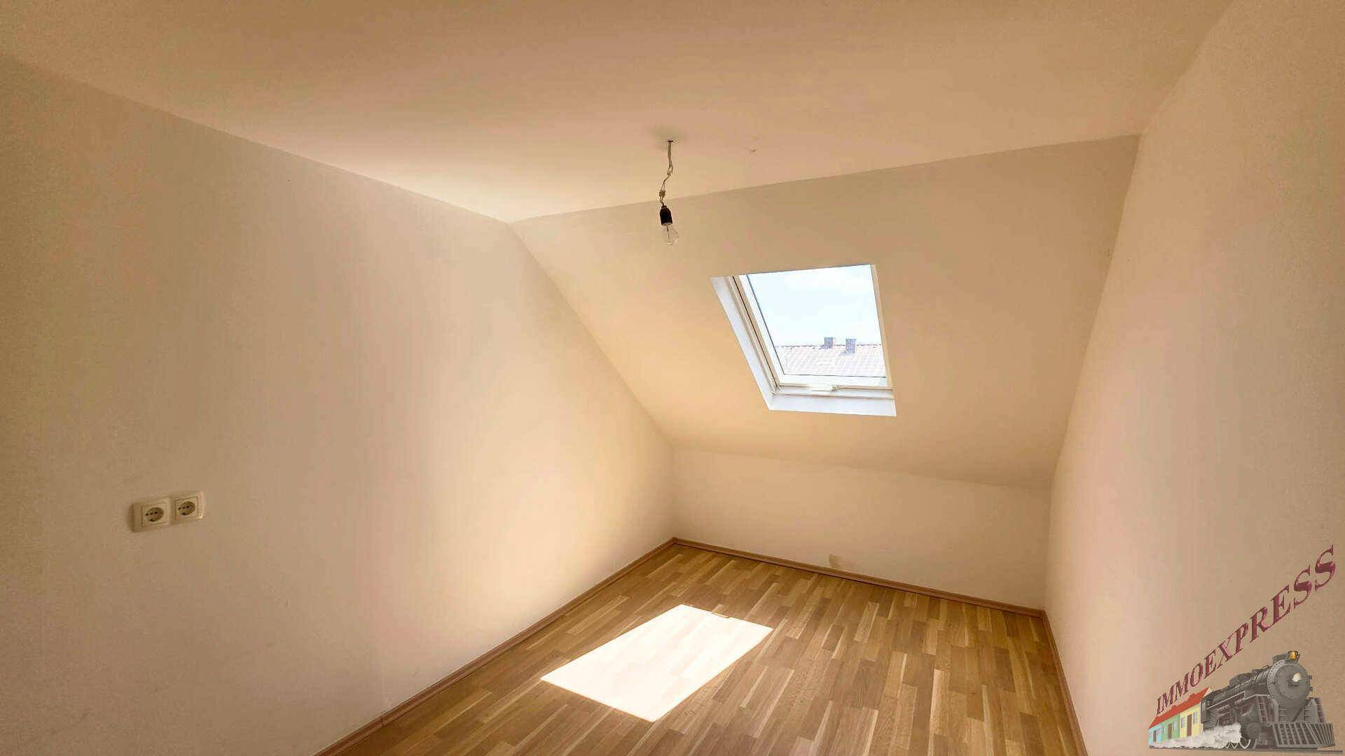 Helles Dachzimmer mit schrägen Wänden, Holzboden und einem Dachfenster für natürliches Licht.