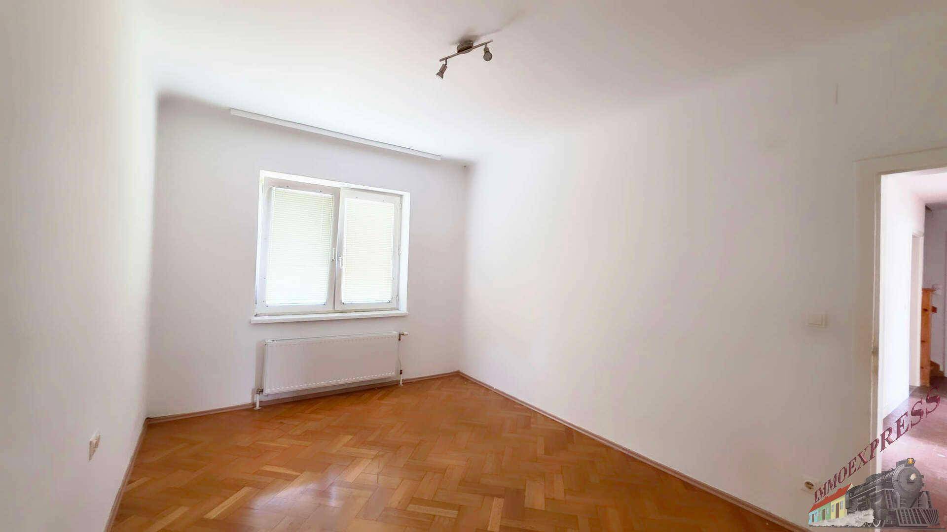 Helles Zimmer mit Fischgrätparkettboden, einem großen Fenster und weißen Wänden.
