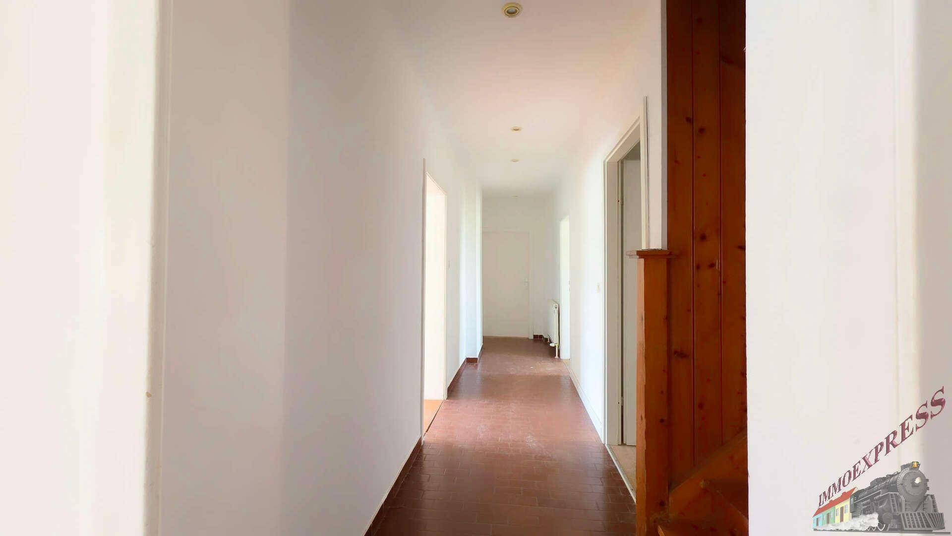 Heller Flur mit dunklem Holzboden, weißen Wänden und einer Holztür, die zu weiteren Räumen führt.