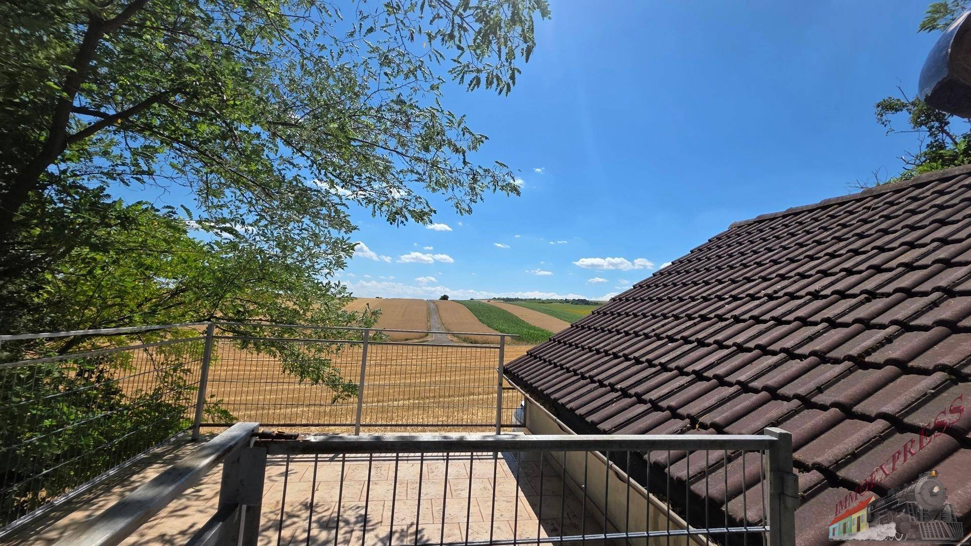 Aussicht von einer oberen Terrasse über die umliegenden Felder und das Ziegeldach.
