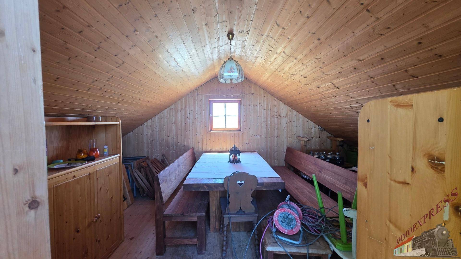 Dachzimmer mit schräger Holzdecke, Holztisch und Bänken, ideal für gesellige Runden.
