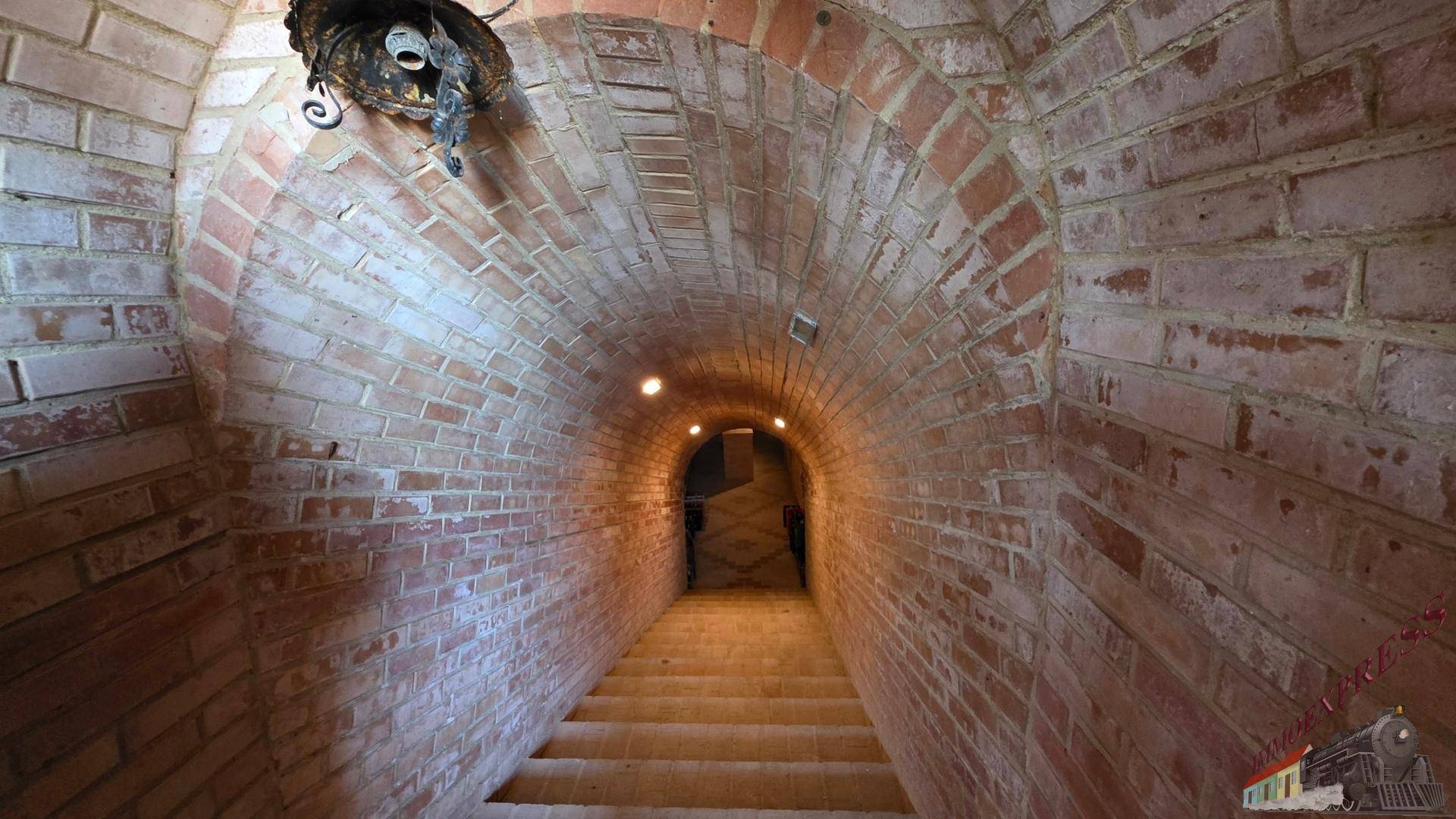 Gewölbter Ziegelgang mit Treppe, die in einen tieferen Kellerbereich führt.