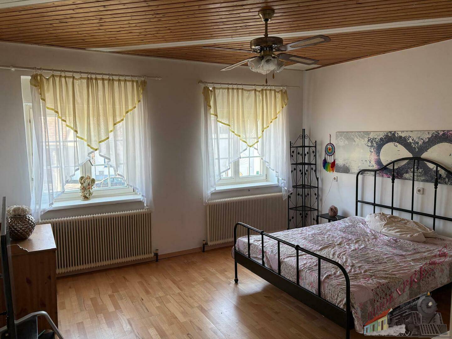 Helles Schlafzimmer mit Holzboden, Holzdecke, Deckenventilator und schmiedeeisernem Bett.