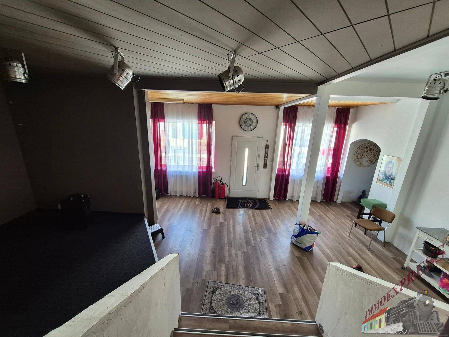 Eingangsbereich mit Holztreppe, Laminatboden und Fenstern mit roten Vorhängen, hell und einladend.