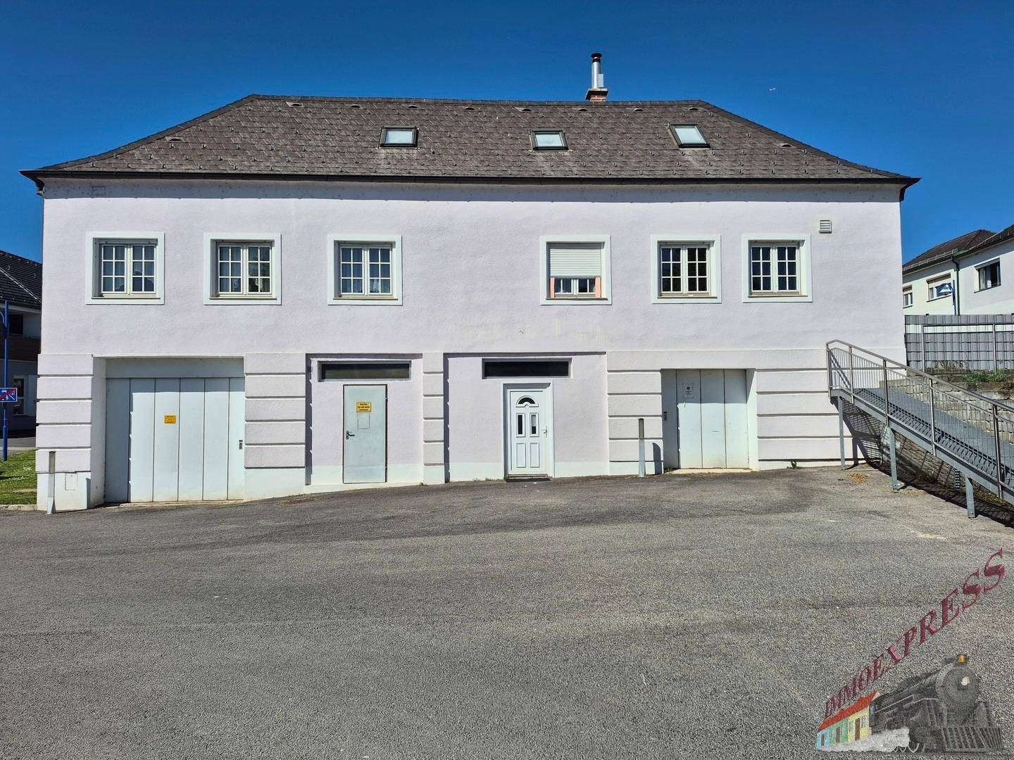 Gebäudeansicht mit mehreren Garagentoren und Fenstern, in heller Pastellfarbe gestrichen.
