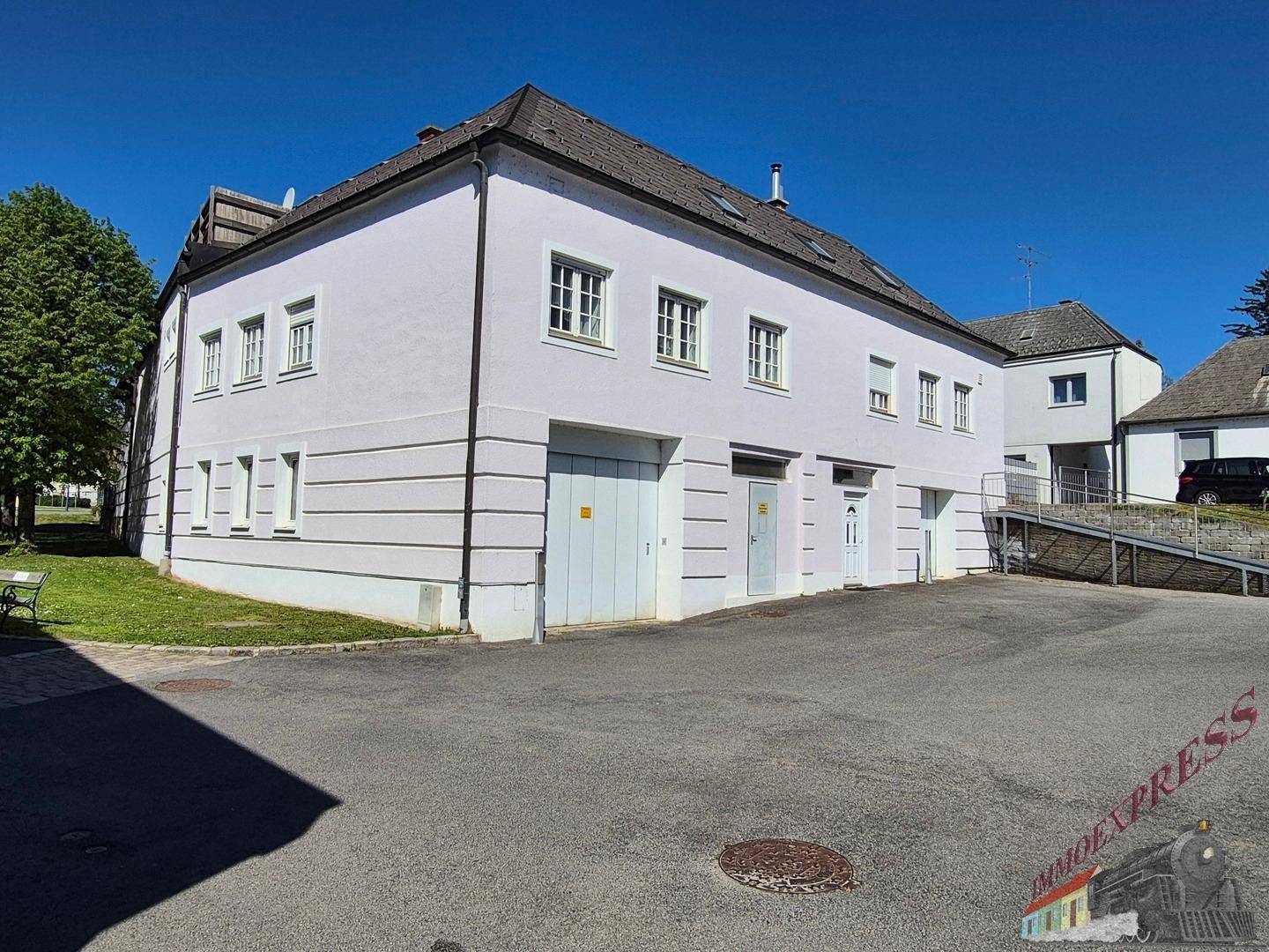 Seitenansicht des Gebäudes mit Garagenzugängen und Rampe, umgeben von Grünflächen.