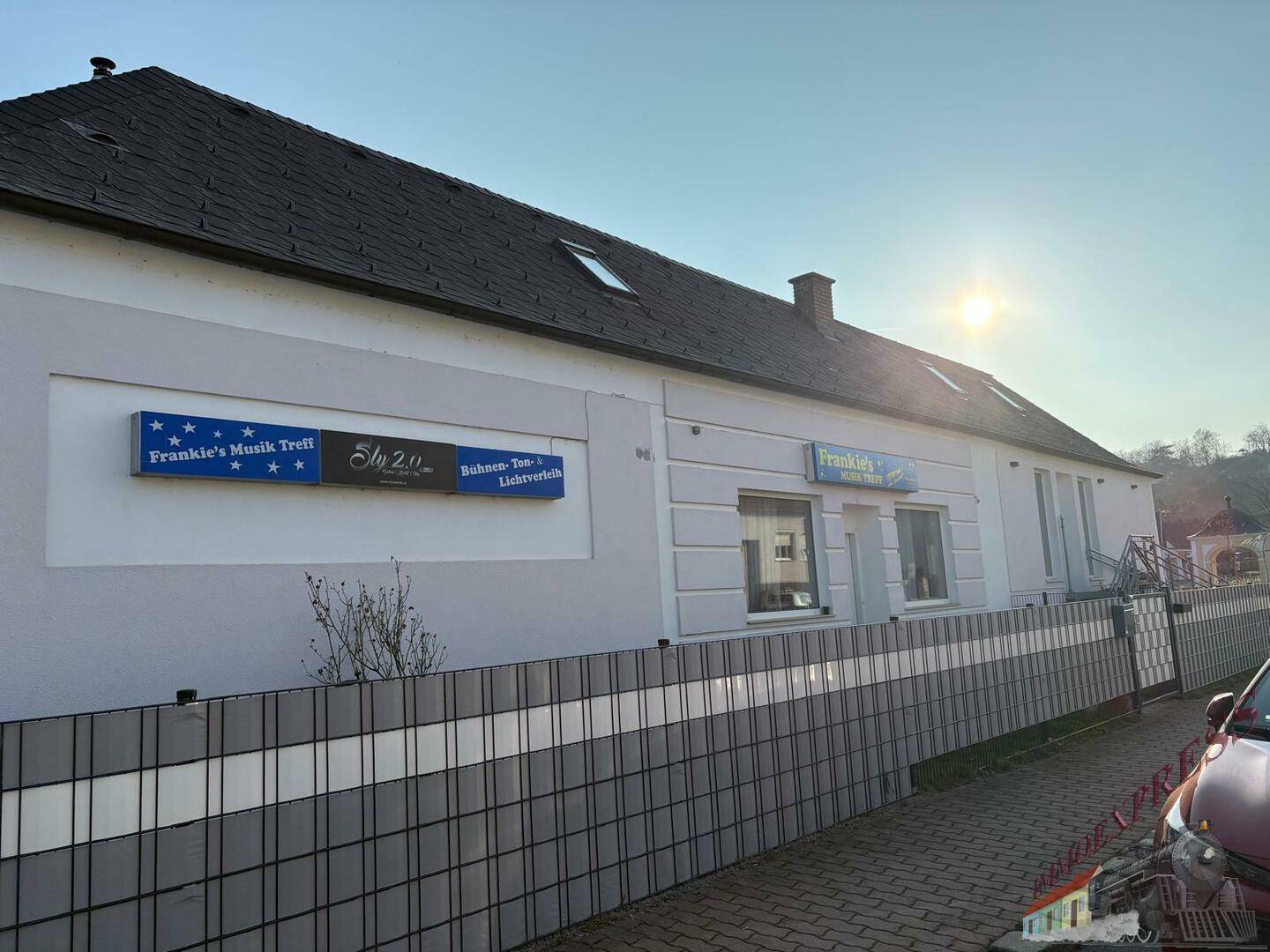 Gebäudeansicht von der Straße mit Werbeschildern und Sonnenschein.