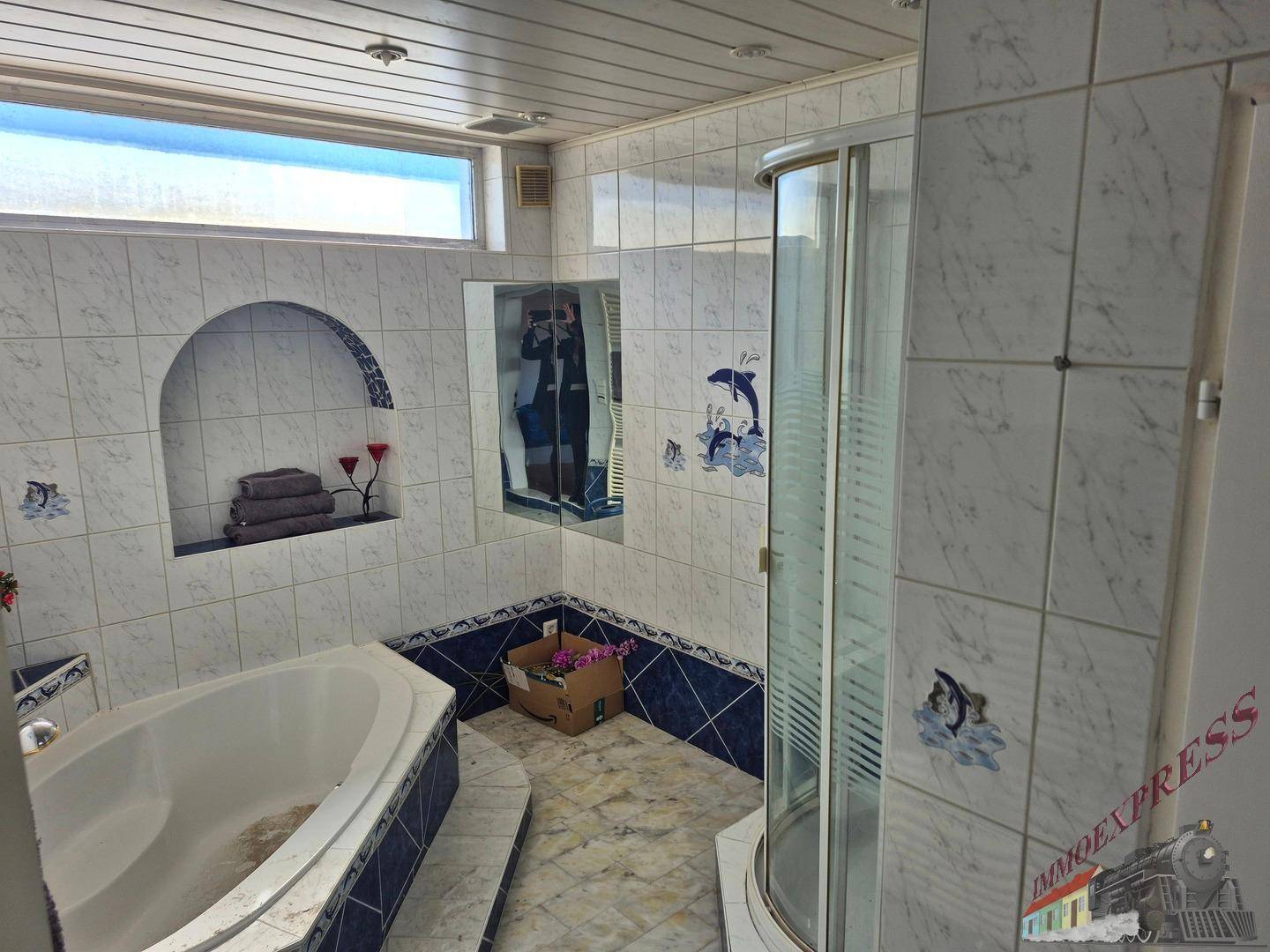 Badezimmer mit Eckbadewanne, Duschkabine und blauen Delfin-Fliesen im 80er-Jahre-Stil.