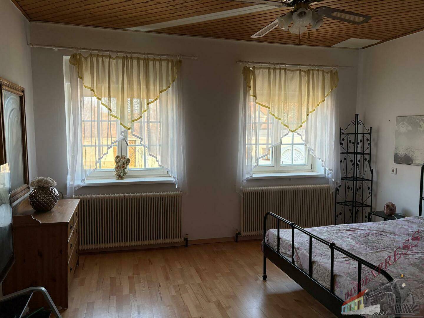 Schlafzimmer mit Holzboden, Holzdecke, zwei Fenstern und einem schmiedeeisernen Bett.