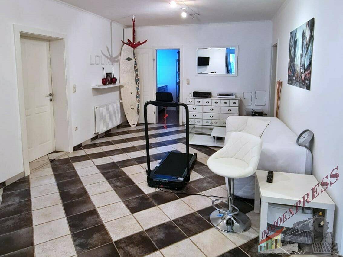 Geräumiger Wohnbereich mit gemustertem Fliesenboden, Laufband und weißer Couch.