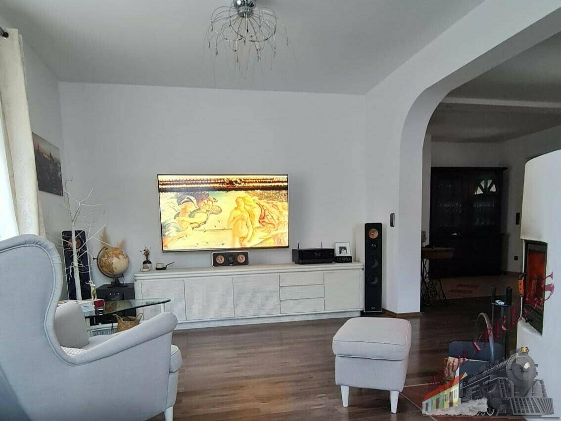 Geräumiges Wohnzimmer mit modernem Entertainment-Center, hellem Parkettboden und elegantem Kronleuchter.