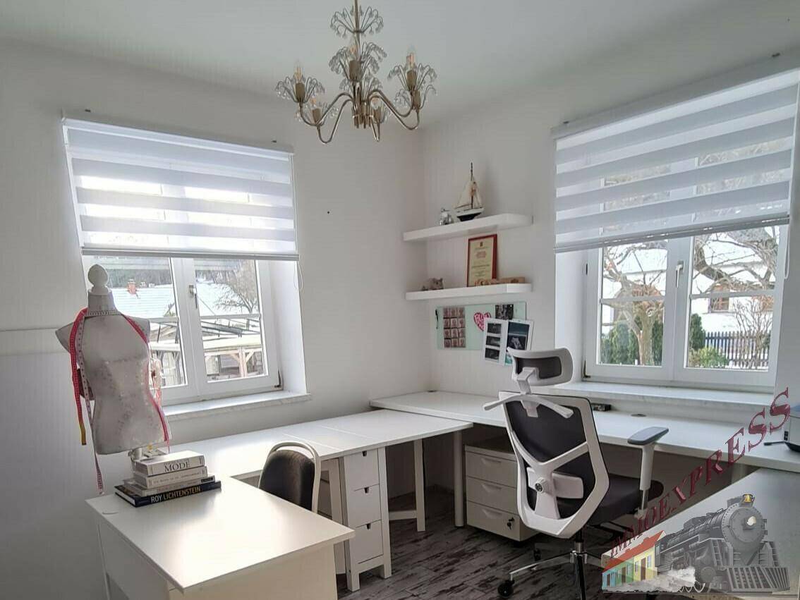 Helles Arbeitszimmer mit zwei Fenstern, großem Schreibtisch und modernem Bürostuhl.