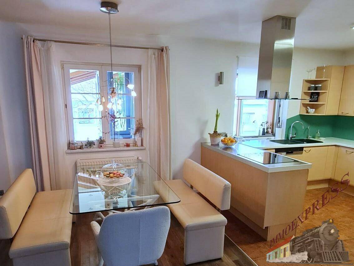 Heller Essbereich mit Sitzbank und Blick auf die moderne Küche mit Kochinsel und Dunstabzugshaube.
