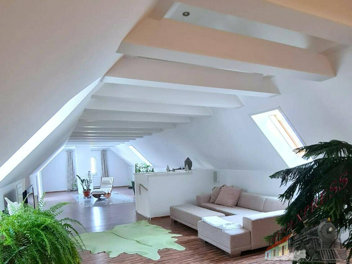 Großzügiger Dachbodenraum mit hohen Decken, Holzboden und Dachfenstern, als Wohnbereich genutzt.