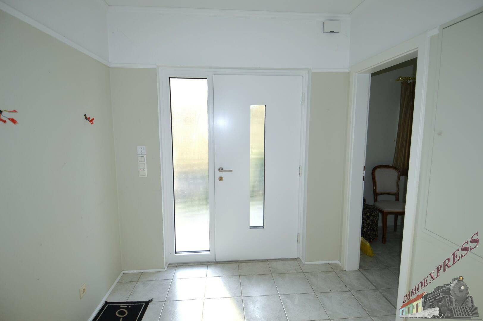 Heller Eingangsbereich mit Fliesenboden und weißer Eingangstür mit Glaseinsatz.